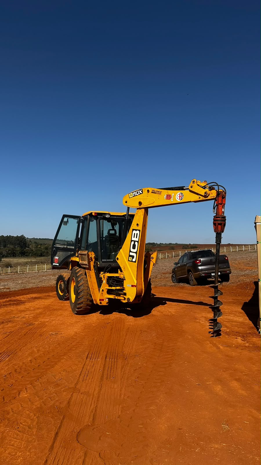 Retroescavadeira JCB com perfuratriz de trado em obra rural